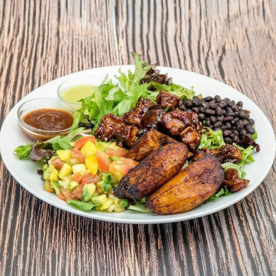 A vibrant plate with glazed chicken, black beans, plantains, avocado salsa, and mixed greens.
