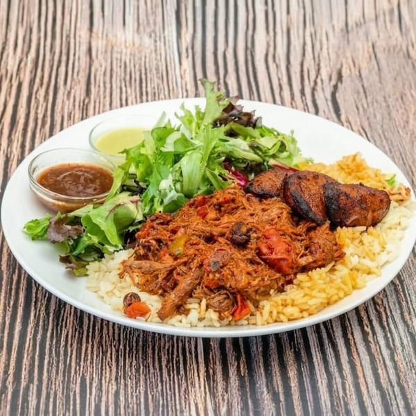 Shredded beef with rice, plantains, and a side salad with two dressings on a white plate.