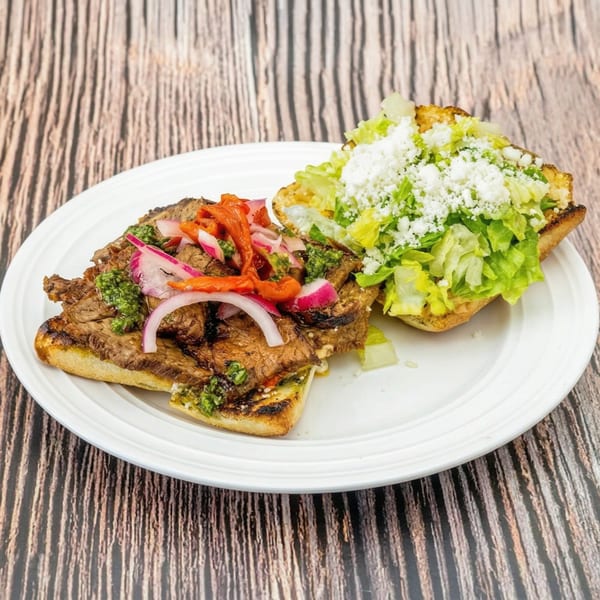 Grilled steak sandwich with pickled onions, red peppers, and green sauce, served with a side salad.