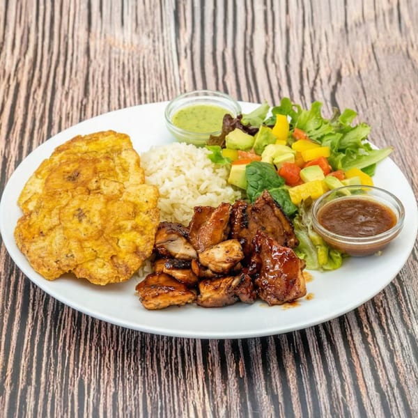 A plate of grilled chicken, rice, fried plantains, and a colorful salad with two dipping sauces.