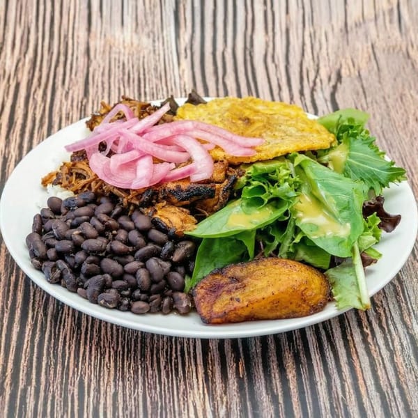 A vibrant bowl with pulled pork, pickled red onions, black beans, salad, and plantains.