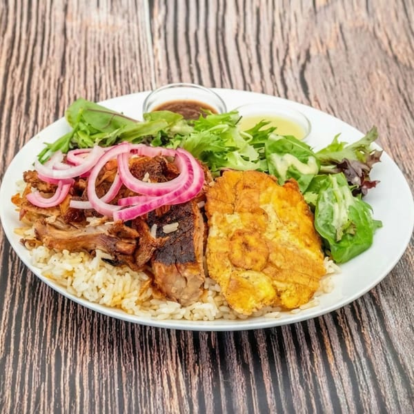 A plate of rice, pulled pork with red onions, fried plantains, and a side salad with dressing.