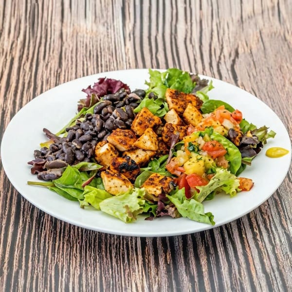 A vibrant salad with grilled chicken, black beans, and salsa on a white plate.