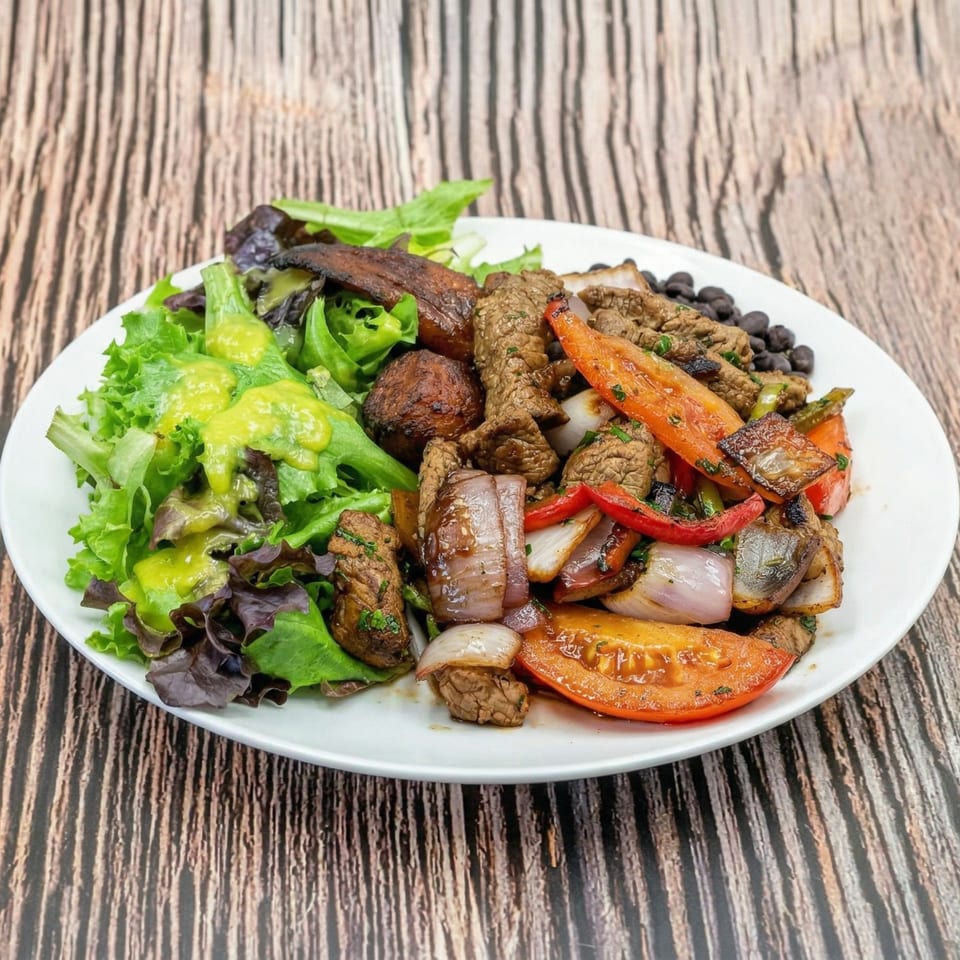 A white plate with steak, onions, tomatoes, black beans, and a green salad with dressing.